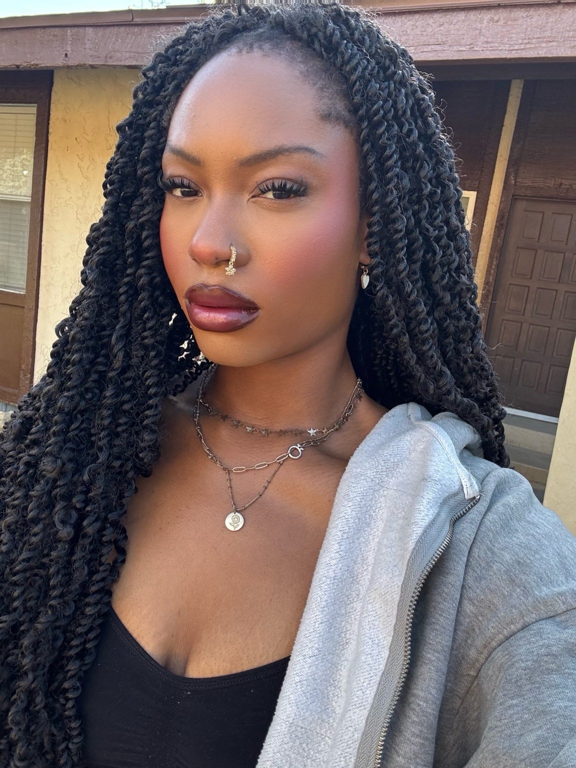 Portrait of Nada Seriu-Aigbokhan with long braids, layered necklaces, and a gray jacket
